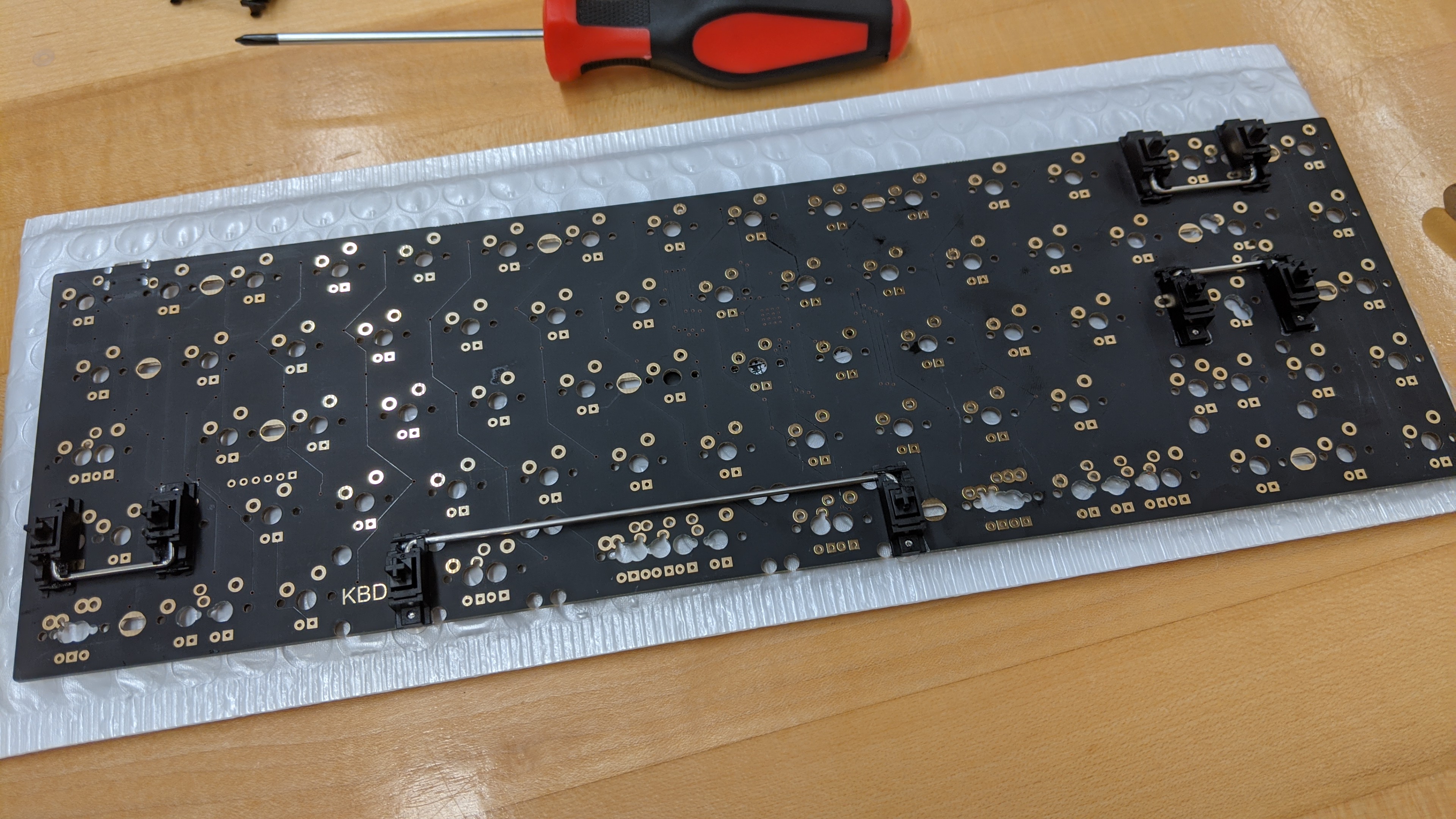 A printed circuit board sitting on a desk. It has small plastic and wire components installed, called stabilizers.'